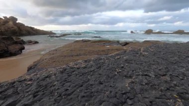 Kayalık uçurum kıyıları ve dalgaların üzerine çöktüğü cennet manzarası. Sörfçü Praia do Castelejo 'daki kayalar Sagres yakınlarında. Portekiz 'in güneyindeki Algarve bölgesinin Batı Atlantik kıyıları.