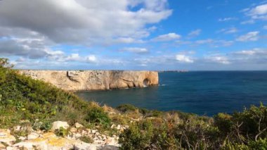 Kayalık uçurum kıyıları ve dalgaların üzerine çöktüğü cennet manzarası. Sörfçü Praia do Castelejo 'daki kayalar Sagres yakınlarında. Portekiz 'in güneyindeki Algarve bölgesinin Batı Atlantik kıyıları.