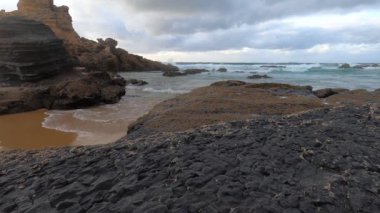 Kayalık uçurum kıyıları ve dalgaların üzerine çöktüğü cennet manzarası. Sörfçü Praia do Castelejo 'daki kayalar Sagres yakınlarında. Portekiz 'in güneyindeki Algarve bölgesinin Batı Atlantik kıyıları.