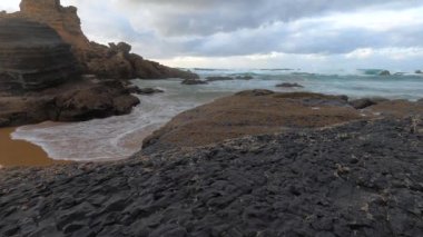 Kayalık uçurum kıyıları ve dalgaların üzerine çöktüğü cennet manzarası. Sörfçü Praia do Castelejo 'daki kayalar Sagres yakınlarında. Portekiz 'in güneyindeki Algarve bölgesinin Batı Atlantik kıyıları.