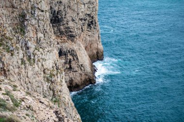 Kayalık uçurum kıyıları ve dalgaların üzerine çöktüğü cennet manzarası. Sagres yakınlarındaki kayalar. Portekiz 'in güneyindeki Algarve bölgesinin Batı Atlantik kıyıları.