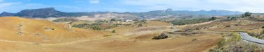 Kırsal kesimdeki panoramik yol manzarası çiftlik arazileriyle çevrili küçük bir köye götürüyor, Ronda, İspanya