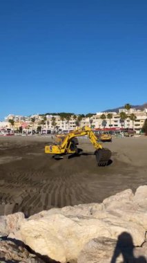 TORREMOLINOS, İspanya - 21 Mayıs 2024: Komatsu kazıcısı 21 Mayıs 2024 tarihinde İspanya 'nın Torremolinos kentindeki kumsaldaki kumu düzleştirir