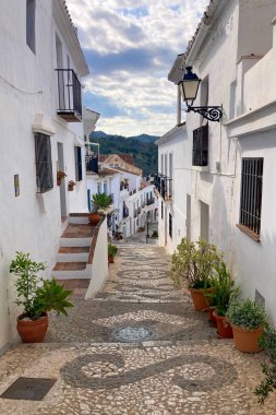 FRIGILIANA, SPAIN - 10 Mayıs 2025: Frigiliana, İspanya 'da beyazlatılmış evler ve renkli çiçeklerle çevrili büyüleyici dar sokaklarda huzurlu bir yürüyüş