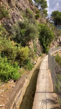 İspanya 'nın Frigiliana kentindeki eski bir sulama hendeği boyunca bir yürüyüş yolundan çevresindeki dağların ve resimli köyün manzarası..