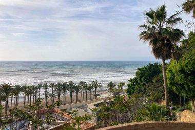 TORREMOLINOS, SPAIN - 30 Nisan 2025: Canlı şehir merkezinden manzaralı deniz geçidine doğru sakin bir yürüyüş yapmak, İspanya 'nın Torremolinos kentindeki büyüleyici sahil atmosferinde ıslanmak.