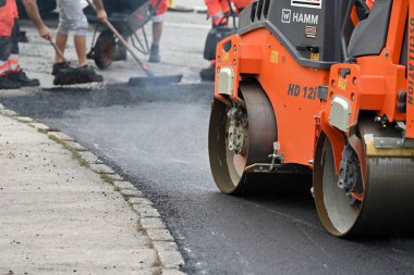 Bir yol silindiri, arka planda işçilerin ayakları.