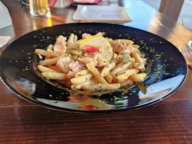 Lezzetli bir tabak makarna, yumuşak tavukla servis edilir ve bir dilim limon ve taze otlarla süslenir. İtalyan mutfak tutkunları ve yemek fotoğrafçıları için ideal..