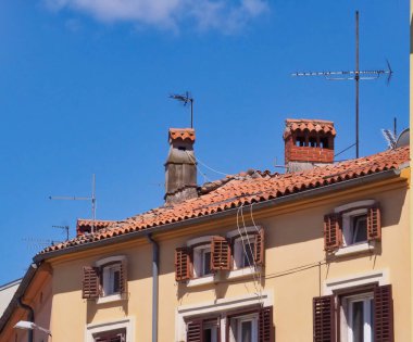 Parlak mavi gökyüzüne karşı terracotta fayansları ve antenleri olan pitoresk bir çatı, Akdeniz mimarisinin cazibesini ve güneşli bir günün dingin atmosferini yakalıyor..