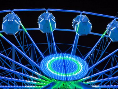 Göz kamaştırıcı bir dönme dolap gece gökyüzünü canlı yeşil ve mavi renklerle aydınlatıyor ve büyülü bir lunapark deneyimi yaratıyor. Eğlence, gece hayatı ve eğlence için mükemmel bir tema..