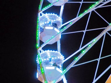 A vibrant view of a Ferris wheel with brightly lit carriages against a dark night sky, showcasing the energy and excitement of an amusement park experience. clipart