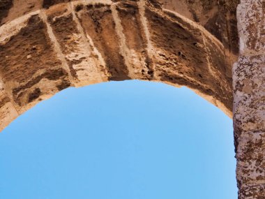 Tarihi mimari ve yıpranmış dokuların sergilendiği canlı mavi gökyüzüne karşı antik bir taş kemerin yakın çekimi. Bu görüntü, mimari tasarımın zamansızlığını ve güzelliğini yakalar..