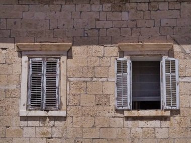 Bu resim, iki klasik ahşap pencereli taştan bir duvarı gösteriyor. Yıpranmış ahşap ve dokulu taş, zamansız bir cazibe ve tarih hissi uyandırıyor..