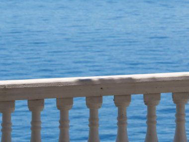 Beyaz bir balkon korkuluğundan görülen, dinginlik ve rahatlama hissi uyandıran derin mavi okyanus manzarası. Seyahat ya da tatil resimleri için mükemmel..