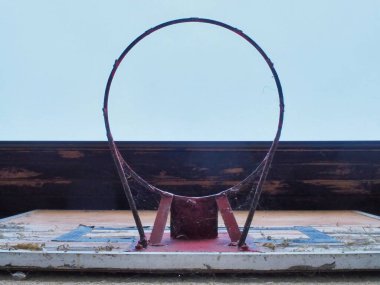 Ağ olmadan yıpranmış ve paslı açık hava basketbol potası, örümcek ağlarıyla çevrili, ihmal ve açık hava sporları ortamında nostaljiyi simgeliyor. Parlak gökyüzü arkaplanı olan eski bir nesnenin aksine.