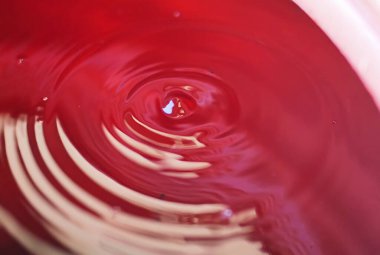 Kırmızı sıvıdaki dalgalanmaların detaylı tasviri, dinamik etkilerini ve hareketlerini gösteriyor. Sıvı hareket ve canlı renkler içeren arka plan veya kavramsal tasarım projeleri için idealdir.