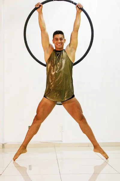 A Mexican male gymnast, performing solo on the aerial ring, displays strength and agility, evoking magnificence and fitness excellence