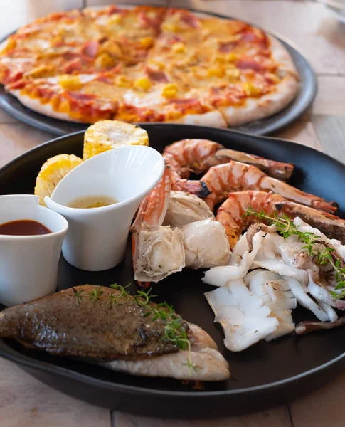 Karışık deniz ürünleri tabağında mavi yengeç, büyük karides, kalamar mürekkep balığı ve limonlu ızgara barakuda balığı var.