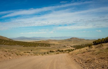 Uçsuz bucaksız Utah çölünü ve uzak dağları gösteren toprak bir yol.