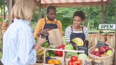 Mutlu Afrikalı erkek ve kadın çiftçilerin portresi marketteki kadın alıcılara poşet dolusu yiyecek veriyor. Organik tarım ürünleriyle tezgahta duran aile işi. İş konsepti