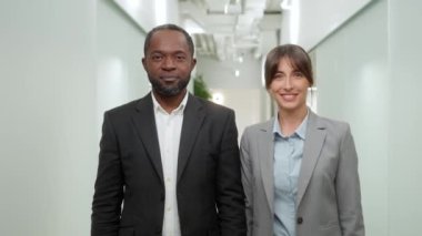 Modern ofiste çalışan iki başarılı meslektaşın portresi. Takım elbiseli yakışıklı Afrikalı bir adam ve kollarını kavuşturup kameraya bakıp gülümseyen güzel bir kadın..