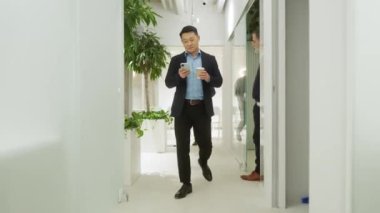 Takım elbiseli yakışıklı Asyalı adamın portresi. İnternette akıllı telefon kullanıyor. Modern şirketin güzel profesyonel çalışanı resmi kıyafetler giyiyor ve elinde bir fincan kahve tutuyor..