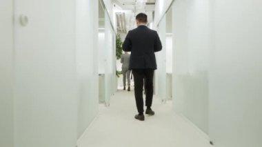 Modern ofis koridorlarında şık kıyafetlerle dolaşan çok ırklı bir grup insan. Genç profesyonel Afro-Amerikan adam telefonla konuşuyor ve yetişkin stili erkek çalışan yürüyor..