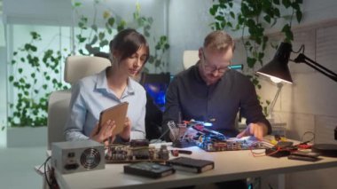 Bilgisayarda çalışan iki genç çalışanın portresi. Tablet kullanan çekici profesyonel kadın asistan başarılı mühendislik lehimleme ana kartına ofisinde yardım ediyor..