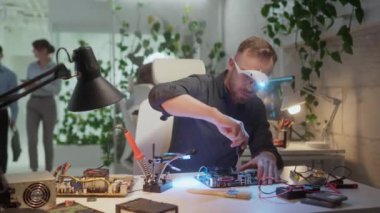 Ofiste oturan bilgisayar parçalarını tamir eden modern servis çalışanı başarılı bir beyaz portresi. Ana kartı tamir etmek için tornavida kullanan dürbün gözlüklü çekici profesyonel mühendis.