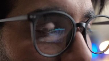 Ekranın yansıması ve ikili kodlu gözlük takan genç adamın yakın plan görüntüsü. Modern bilişim şirketinin ofisinde bilgisayar üzerinde çalışan profesyonel erkek geliştirici..