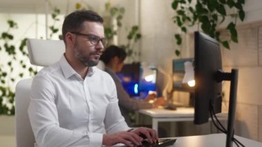 Ofiste çalışan bilgisayarlı klavyeyle yazı yazan profesyonel bir portre. Beyaz gömlek ve gözlük takan çekici odaklı beyaz tenli teknik eleman..