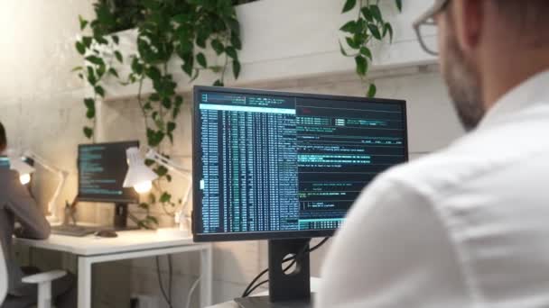 年轻专业成功的男性程序员在计算机上编写二进制代码的背对背视图 在现代公司工作的专注的高加索人开发人员 穿着衬衫在办公室工作 — 图库视频影像