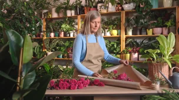 Umtriebige Glückliche Grauhaarige Floristin Die Blumensträuße Mithilfe Eines Blumenwicklers Lächelnd — Stockvideo