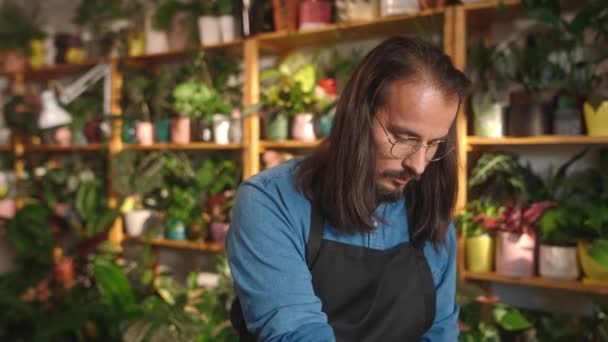 花店柜台上照料土壤和植物的年轻而有魅力的专业男性花匠的画像 在花店工作的漂亮而专注的长胡子成年人 — 图库视频影像