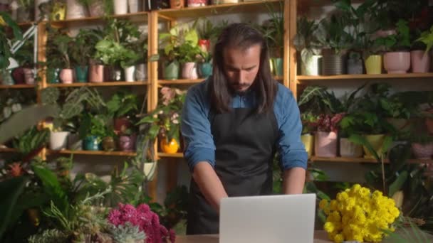 年轻英俊的现代男性花匠在花店网上工作 用笔记本电脑在柜台上做一束漂亮的花 在花卉领域工作的有吸引力的高加索成年人 — 图库视频影像