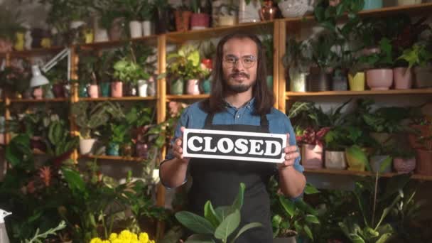 站在花店的美丽的专业男性花匠的画像 展示了戴着围裙和眼镜的封闭标志 成功的男工微笑着看着相机 植物概念 — 图库视频影像