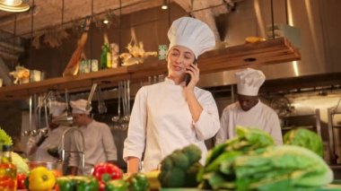 Lezzetli yemekler pişirmeden önce telefonla konuşan ünlü kadın şefin portresi. Çekici, yetenekli bir kadın aşçı olarak çalışıyor modern şık restoran mutfağında malzeme sipariş ediyor..