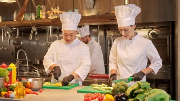 两个有吸引力的专业厨师在餐厅的现代厨房用刀切蔬菜 美丽的高加索女性和熟练的亚洲男性厨师 会说话和做饭 — 图库视频影像