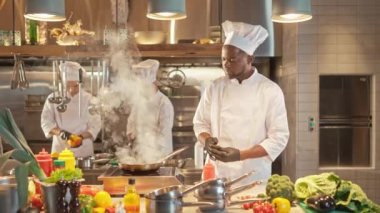 Afro-Amerikan güzel profesyonel şefin portresi tavada kızartılmış ve karıştırılmış sebzeler pişiriyor. Yakışıklı, yetenekli bir aşçı. Modern bir restoranda çalışıyor. Üniforma giyiyor..