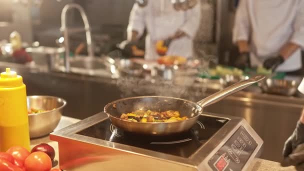 부엌에서 유니폼을 장갑을 요리사가 프라이팬에서 맛있는 야채를 튀기는 모습을 가까이 — 비디오
