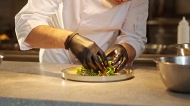 Tabağa koyulan güzel lezzetli salatanın yakın plan portresi ve üniformalı ve siyah eldivenli beyaz bir şef tarafından süslenmiş. Mutfak konsepti.