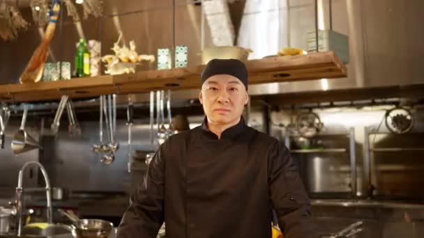 有自信 严肃的亚洲厨师的画像 看着相机 身穿黑色制服 戴着黑色手套 在高档餐厅现代厨房工作的有魅力的专业男性厨师 — 图库视频影像