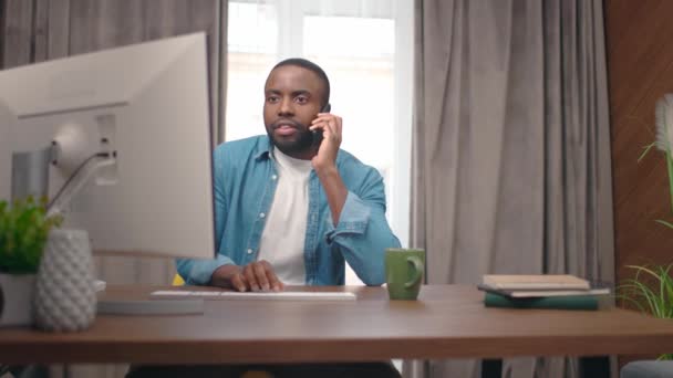 Afroamerikansk Vuxen Man Sitter Framför Monitorn Och Pratar Mobiltelefon Med — Stockvideo