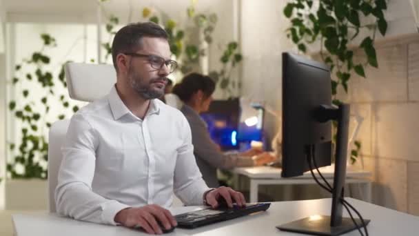 在现代It公司工作的专业英俊男人的肖像 利用计算机开发看着相机微笑 办公室里穿着眼镜和衬衫的有魅力的快乐男性员工 — 图库视频影像