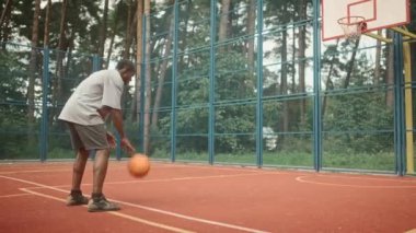 Yetişkin Afro-Amerikan sportif erkek basketbol topunu potaya atıyor. Basketbol oynayan profesyonel oyuncunun arkası potaya vurdu. Açık hava mahkemesi. Park 'taki şehir çocuk parkı