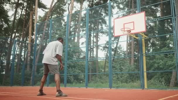 一个成熟的家伙打篮球时的后腿弹跳 把球抛进篮筐里 身穿运动服的非裔美国成年人站在城市体育馆外练习篮球 体育生活方式 — 图库视频影像