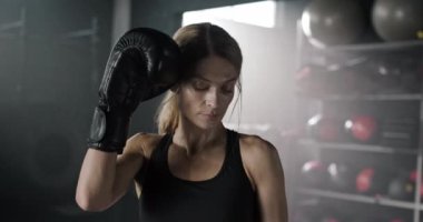 Beyaz kadın portresi, spor salonunun arka planında kameranın önünde duran, spor tişörtü giyen ve boks eldiveni giyen. Eğitimden sonra yorgun görünen güzel bir kadın..