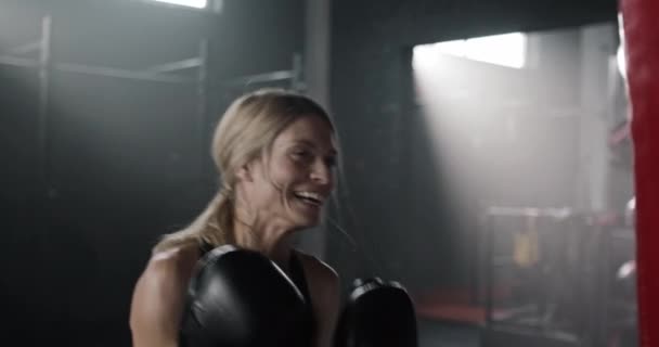 白人妇女积极殴打打斗袋 美丽的女性 身材匀称 面带微笑 练习拳击 在健身房锻炼 力量的概念 — 图库视频影像