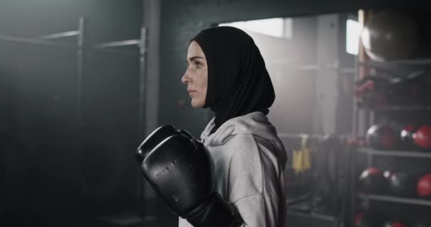 在黑暗的健身室里 女运动员站在拳击台上 严肃地看着镜头的画像 体能训练后 穿着风帽和运动服的漂亮女拳击手看上去棒极了 — 图库视频影像