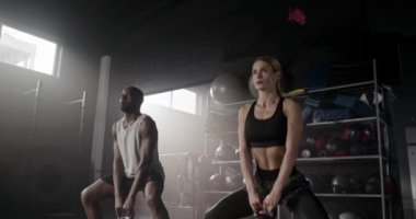 Gölge fitness merkezinde spor giyim eğitimi almış çok ırklı çekici bir çifti uzaklaştırmak. Tapılası insanlar yoğun bir şekilde kettlebell ağırlıklarıyla çömeliyor. Güçlü insanların kasları vardır.